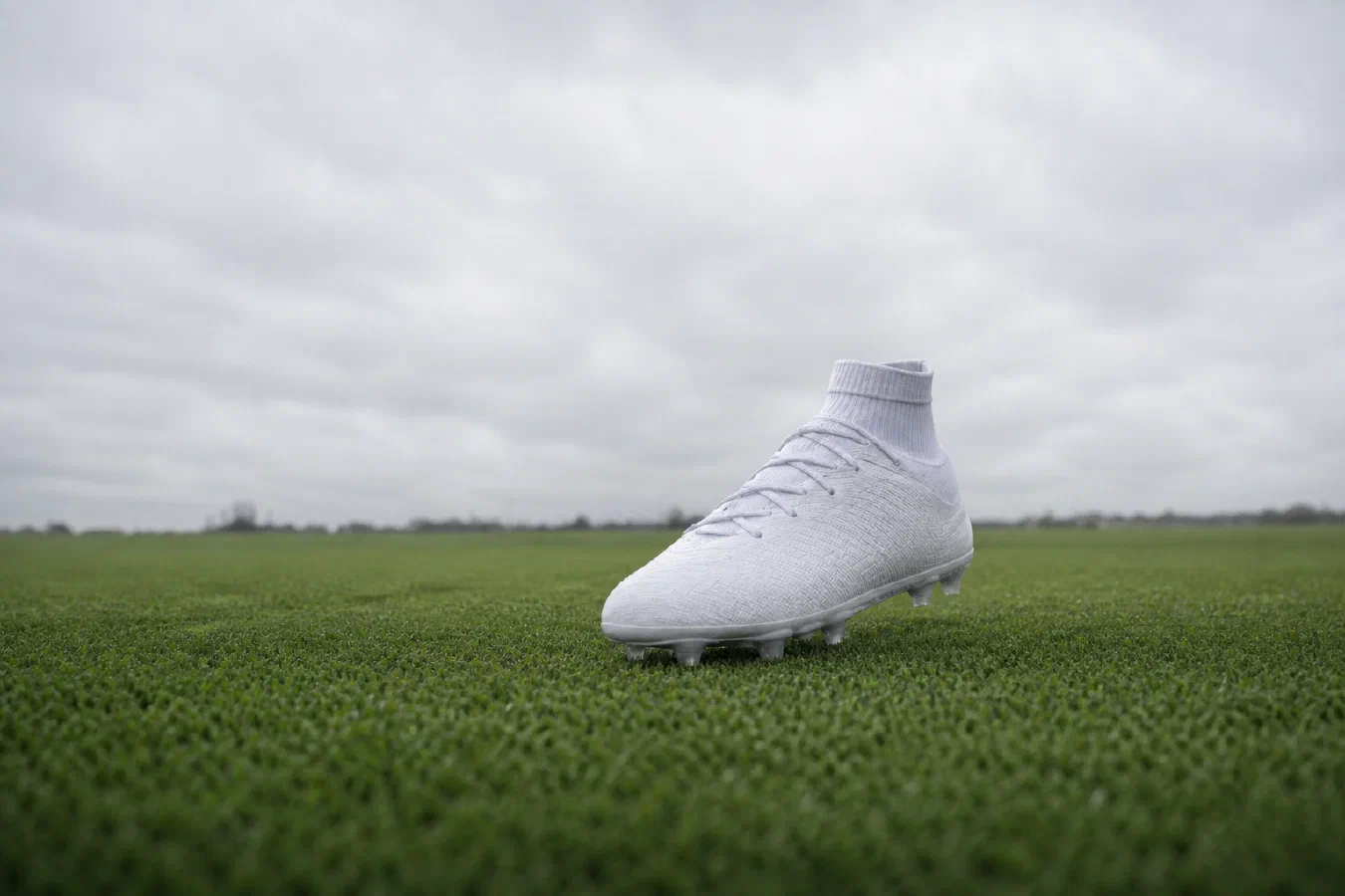 Full unbranded white football boot on a grass pitch